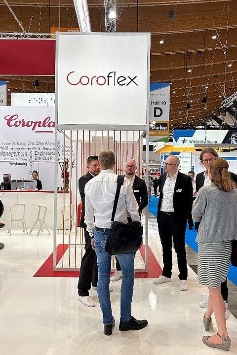 Menschen stehen am Ausstellungsbereich von Coroflex auf der Battery Show 2024 und sprechen miteinander