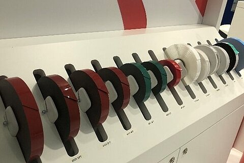 Messestand mit nebeneinander aufgereihten Rollen technischer Klebebänder von Coroplast Tape in verschiedenen Farben und Ausführungen.